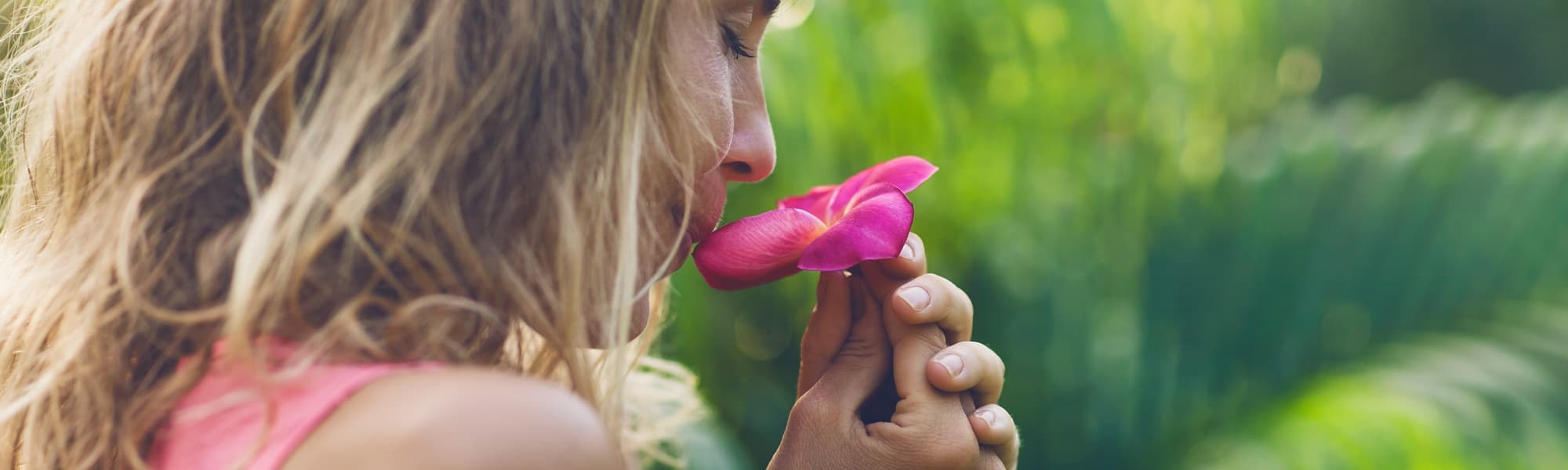 Frau riecht an einer Blume im Sommer. Naturheilmittel können die Gesundheit von Frauen unterstützen.